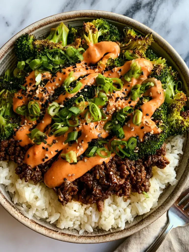 Beef and Broccoli Bowls with Creamy Sriracha Mayo and Jasmine Rice 1 Close up of beef and broccoli bowls showing the artistic zigzag drizzle of creamy orange sriracha mayo and sesame seeds.