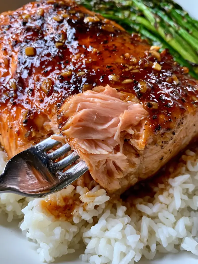 Plated brown sugar salmon with visible minced garlic bits and fresh parsley, served with roasted asparagus.