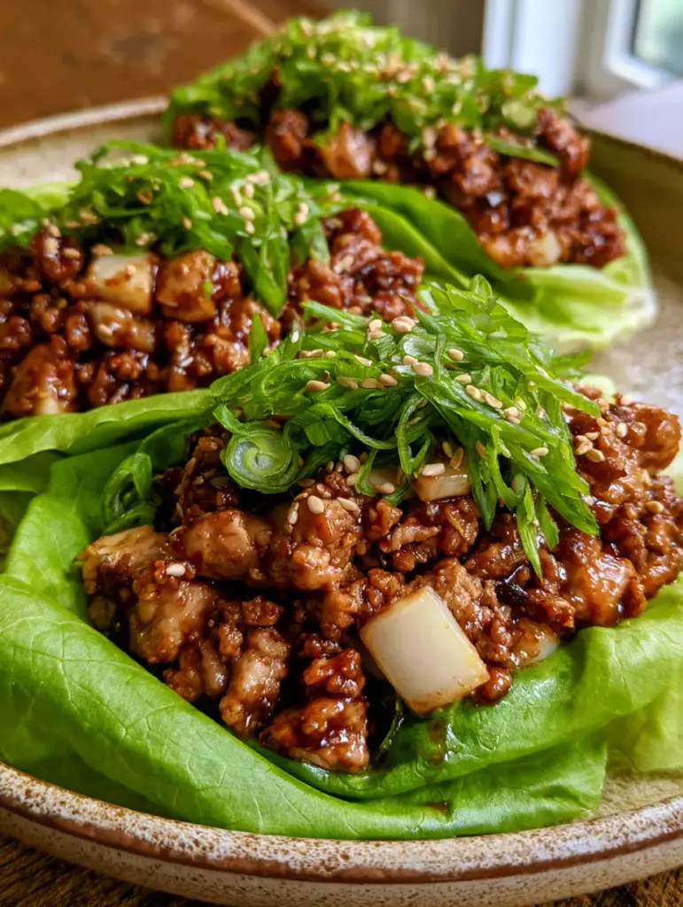 Chicken Lettuce Wraps with a Savory Hoisin Glaze and Crisp Butter Lettuce 1 Close up of ground chicken filling with water chestnuts and green onions in a bright green butter lettuce leaf.