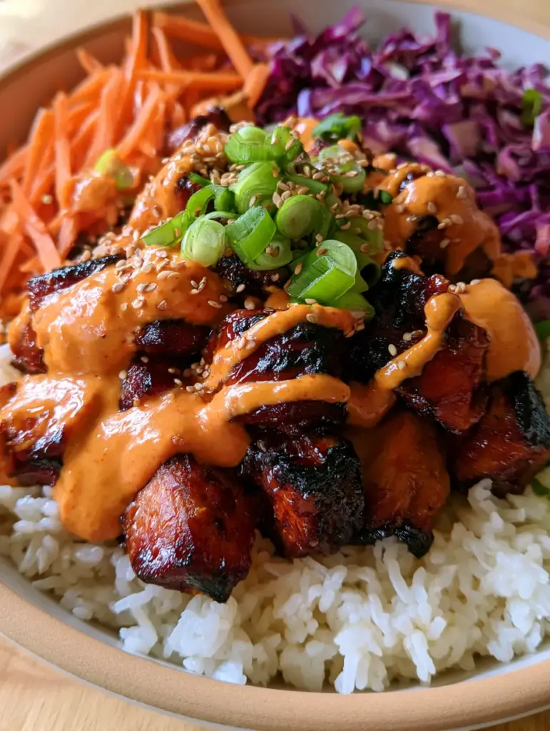 A full Korean BBQ chicken bowl showing julienned carrots, shredded cabbage, and creamy sauce drizzle.