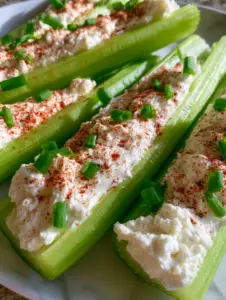 High-angle macro photo of vibrant green celery stalks filled with fluffy whipped white cream cheese, dusted with smoky paprika. (cream cheese stuffed celery)