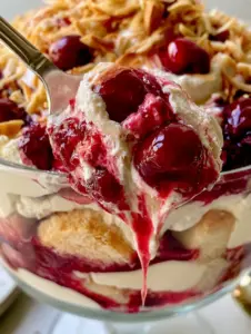 Close-up of a silver spoon scooping a portion of cherry dream dessert with a luscious cherry sauce drip.