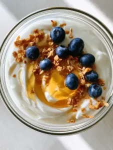 Overhead shot of thick creamy pressure cooker yogurt in a glass bowl with a honey swirl and blueberries.