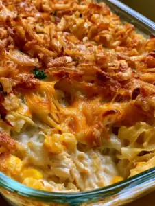 Top-down view of a golden-brown chicken noodle bake with glistening crispy onions and pockets of melted cheddar cheese.