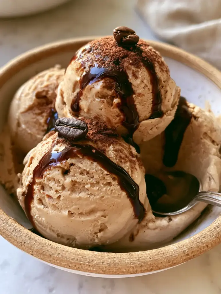 Espresso Gelato: The Ultimate Silky Italian Coffee Dessert 2 A close-up handheld photo of espresso gelato with a silver spoon and glistening dark glaze.