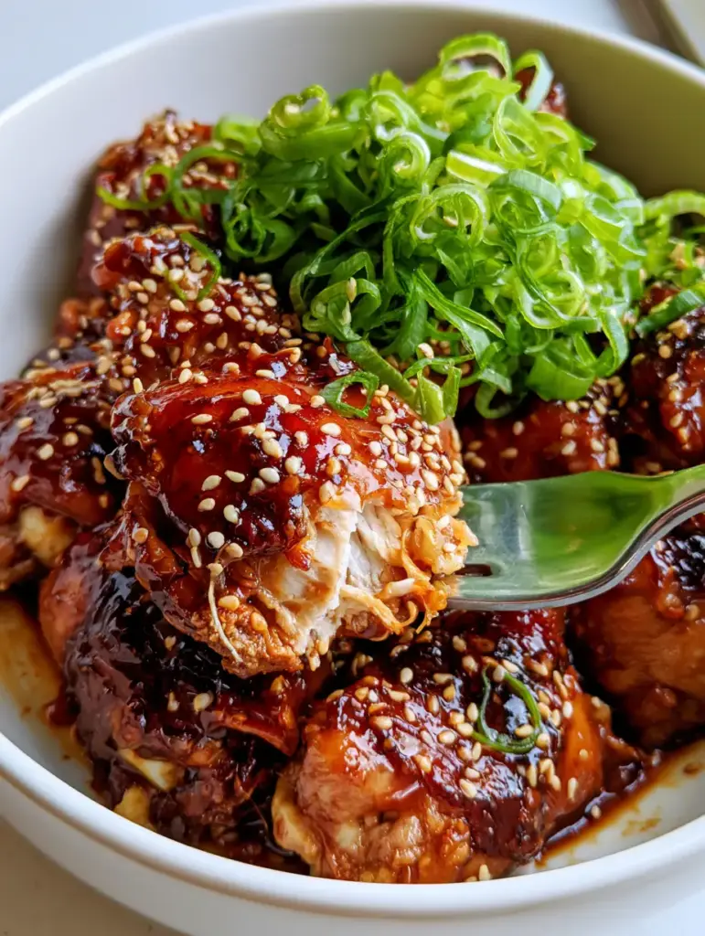 A mountain of curly green scallions on top of mahogany colored slow cooker chicken thighs in a white bowl.