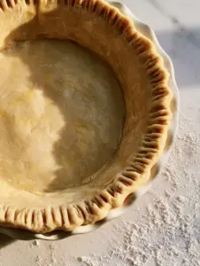 Extreme close-up of raw pie crust dough showing marbled golden butter flecks and fluted edges. (pie crust)
