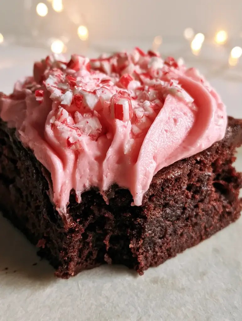 Close-up shot of a pink frosted peppermint brownie with crushed candy canes on a slate surface.