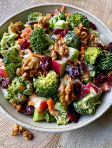 Close-up of fresh broccoli apple salad showing glistening creamy dressing and crimson cranberries.